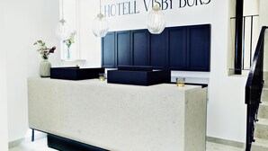 A modern hotel reception area with a large, light-colored reception desk, two hanging pendant lights, and a wall-mounted sign that reads "HOTEL VISBY BÖRS". - Hotell Visby Börs (Visby)
