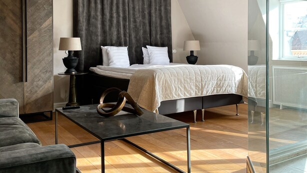 A modern bedroom with a large bed, a smaller bed, a glass partition, and a wooden ceiling. - Hotell Visby Börs (Visby)