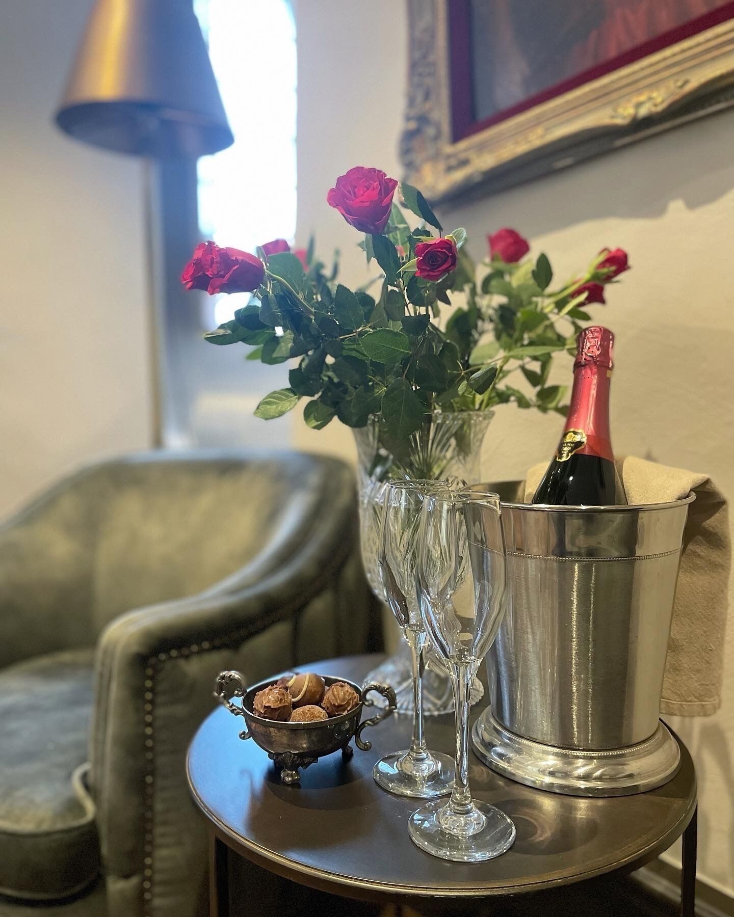 A table with a vase of roses, a bottle of champagne, and a small bowl of nuts.