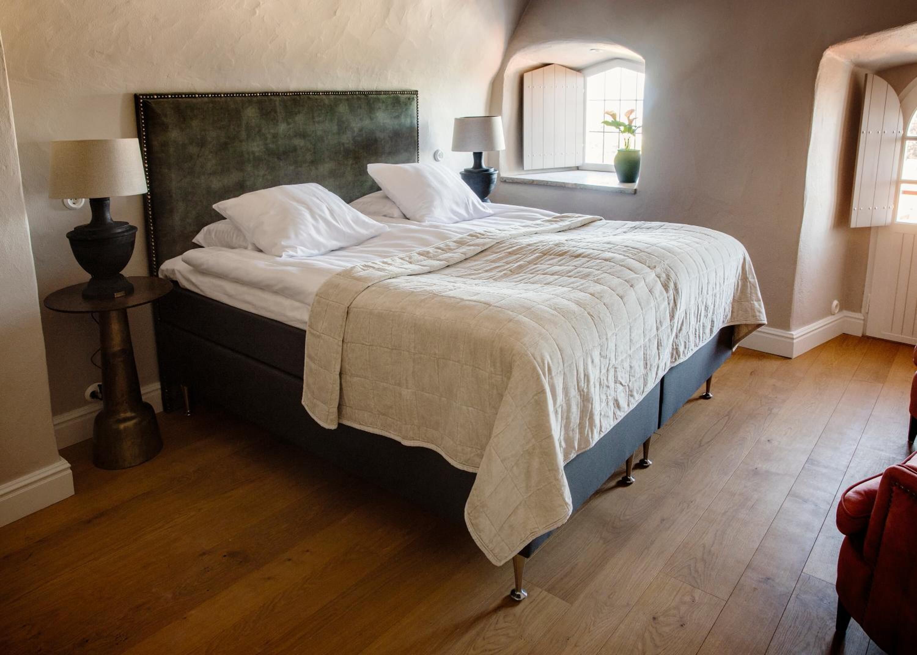A bedroom with a bed, bedside lamps, a window with a view, and a red chair.