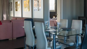 A modern hotel room with a glass dining table, white chairs, a pink sofa, and abstract wall art. - Virgo Loft  Spectacular Acropolis View (Athens)
