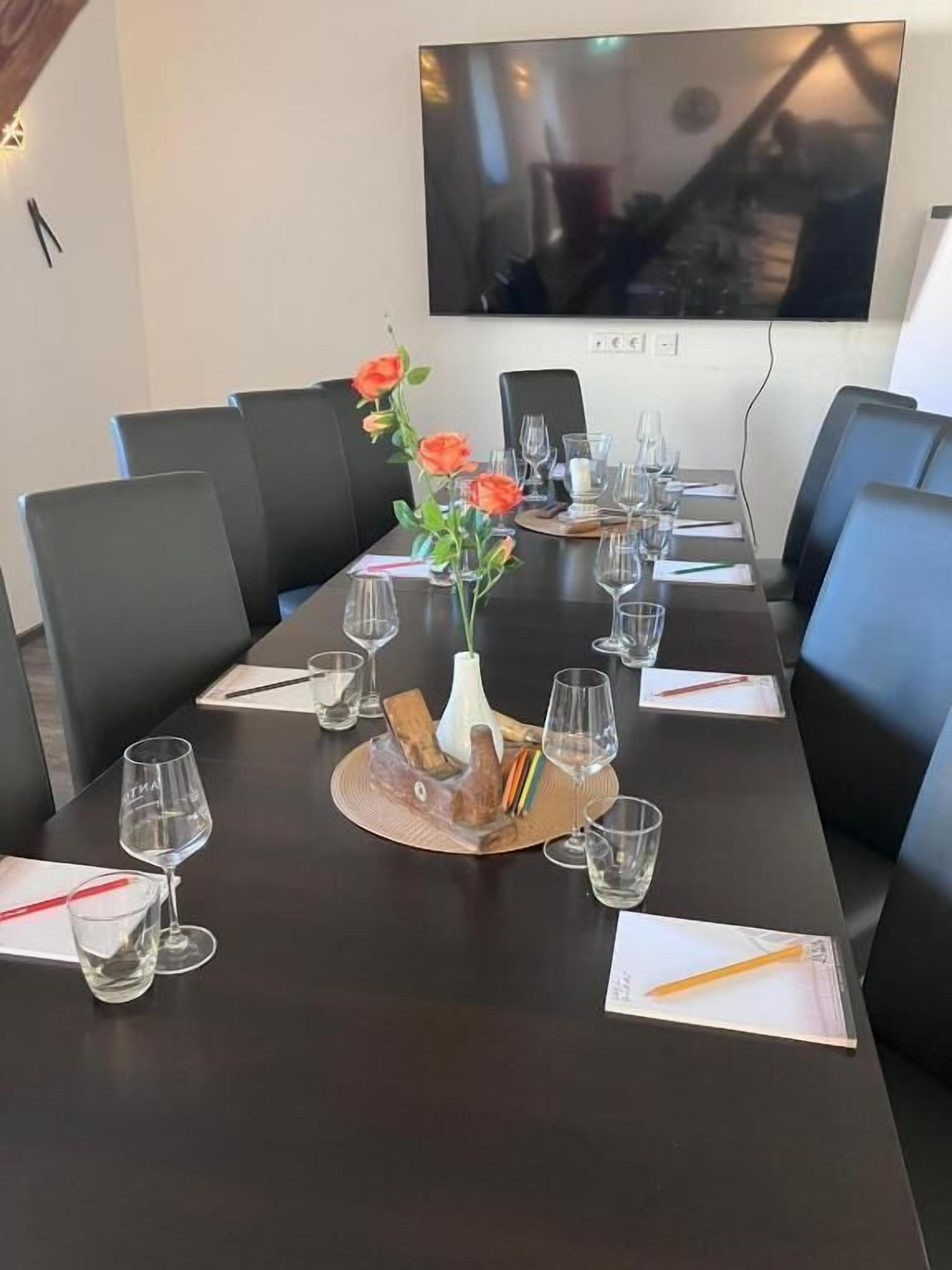 A conference table set with wine glasses, a vase with flowers, and a notepad.