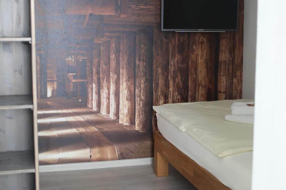 A bedroom with a wooden wall panel, a bed, and a TV mounted on the wall.