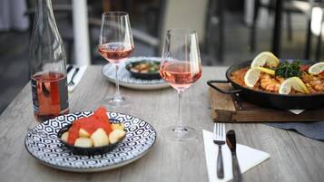 Una mesa de comedor con una botella de vino tinto, dos copas de vino, un plato con comida y una sartén con un guiso decorado con rodajas de limón.