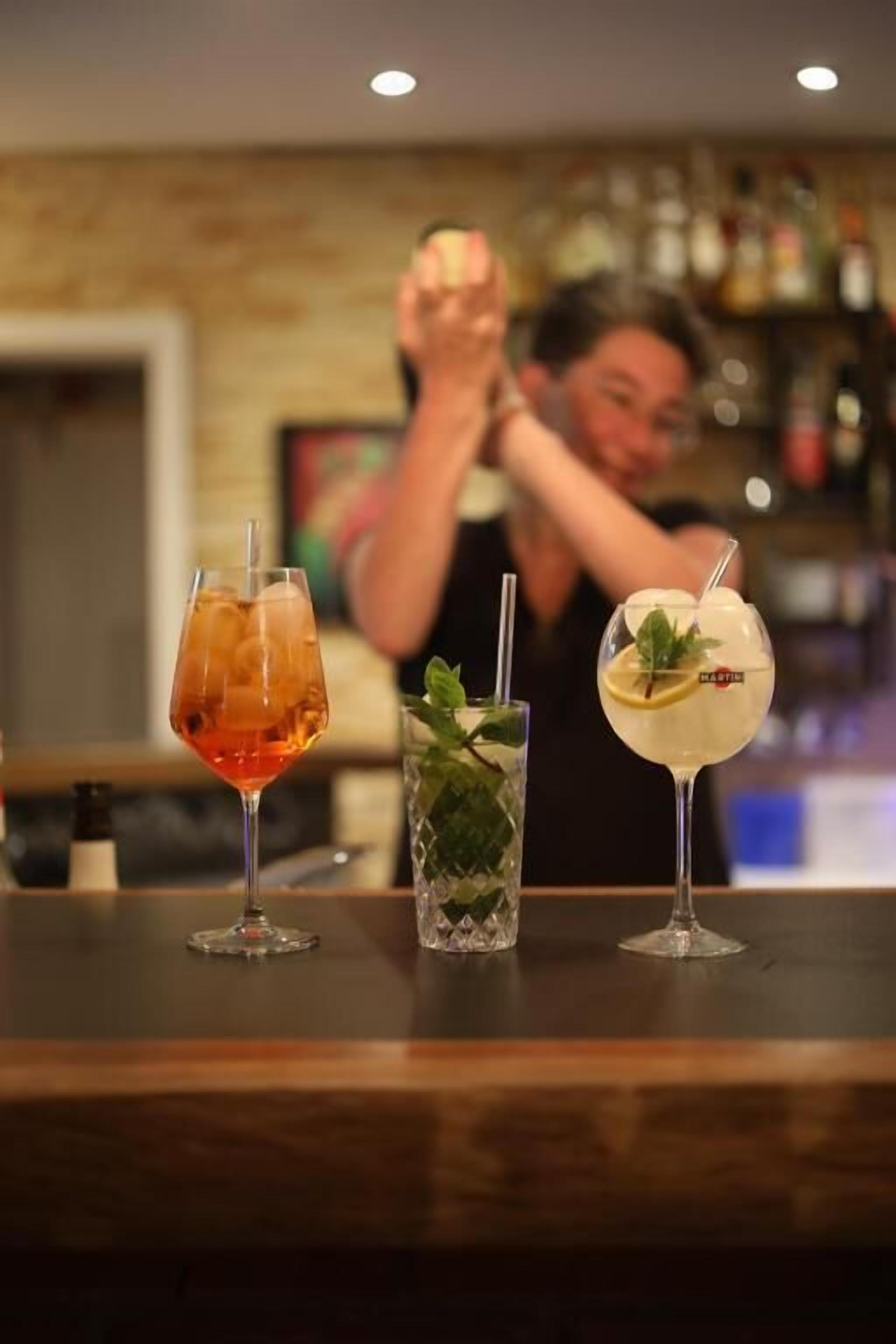 Trois cocktails sont posés sur le comptoir d’un bar, avec un barman en arrière-plan.