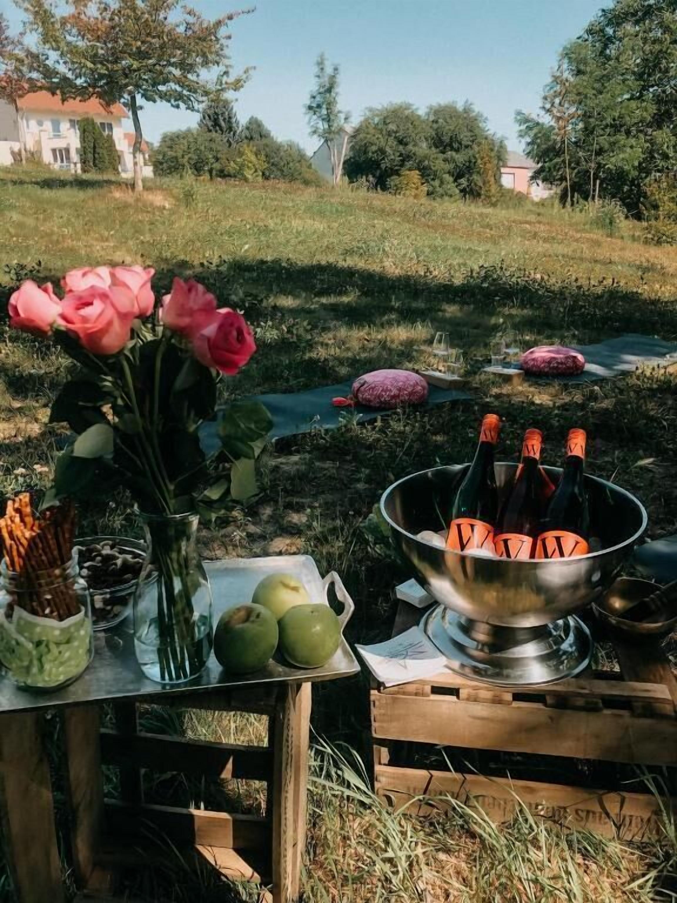 Et bord med en metalkurv, der indeholder flasker, en vase med blomster og en tallerken med mad.