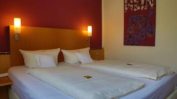 A hotel room with two beds, each with white bedding and pillows, and two wall-mounted lamps.