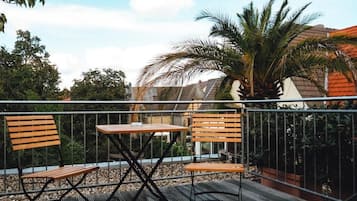 A balcony with wooden chairs and a table, surrounded by a metal railing.