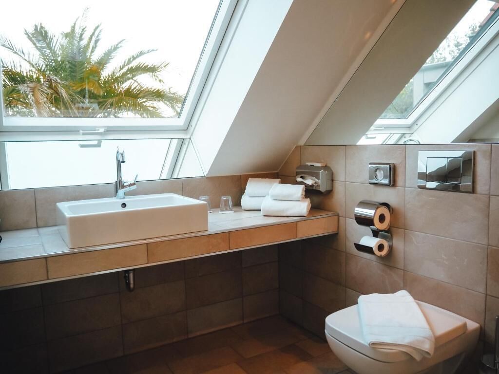 A modern bathroom with a skylight, a sink, a toilet, and a towel dispenser.
