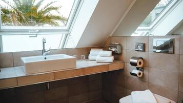 A modern bathroom with a skylight, a sink, a toilet, and a towel dispenser.