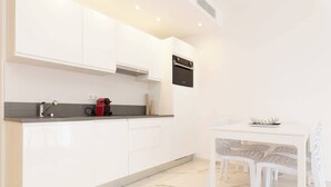 A modern kitchen with white cabinets, a built-in oven, and a dining area with a white table and chairs. - Brand new 2 bedrooms next to Croisette ! (Cannes)