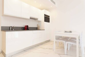 Une cuisine moderne avec des armoires blanches, un four encastré et un coin repas comprenant une table et des chaises blanches.