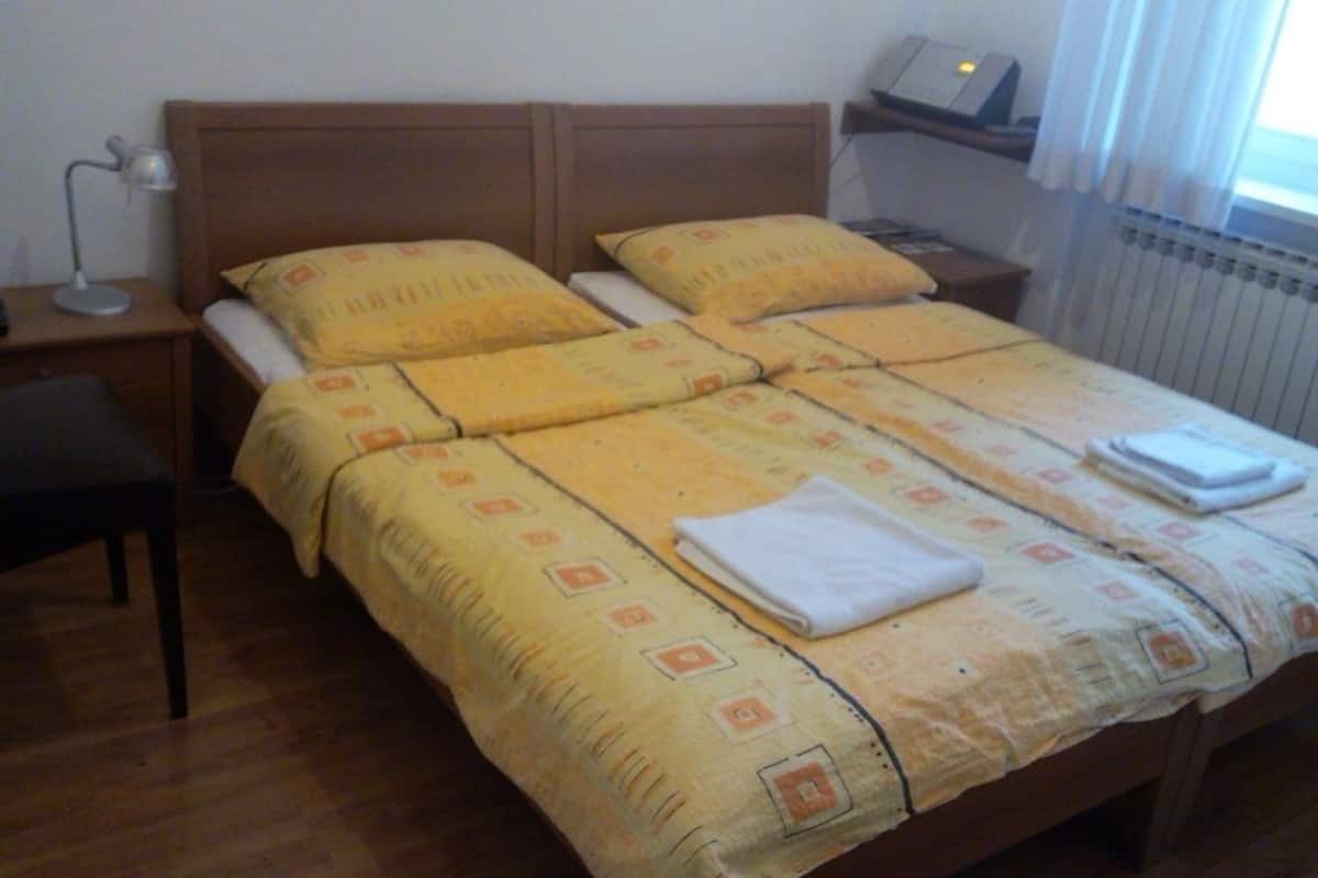 A double bed with a yellow patterned bedspread, a bedside table with a lamp, and a window with curtains.