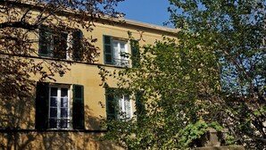 A two-story building with a yellow facade, green shutters, and a stone base. - Cottage in a 1850 Bastide with infinity pool et counter current swimming system  (Eyguières)