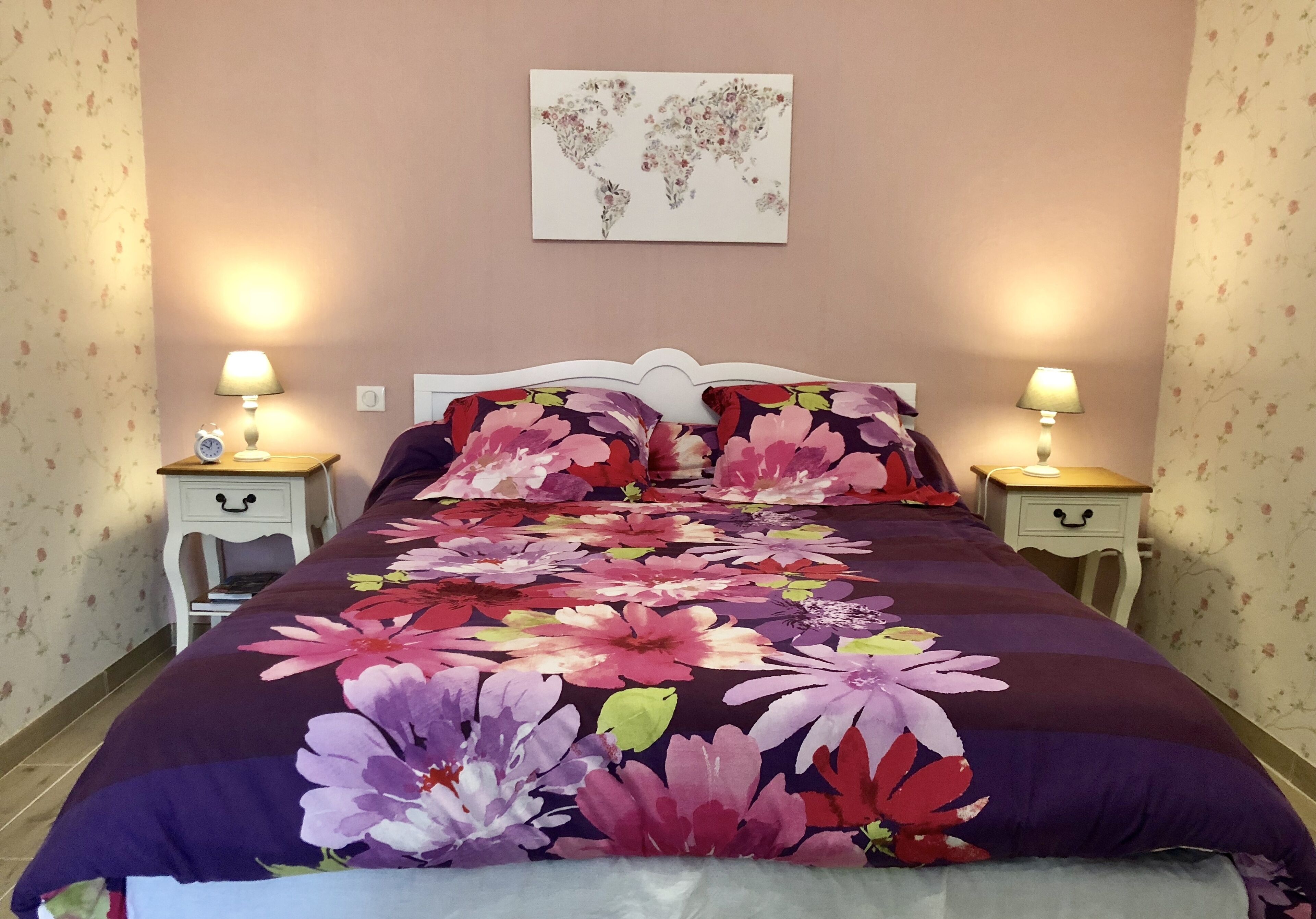 A bed with a floral bedspread, two bedside tables with lamps, and a world map on the wall.