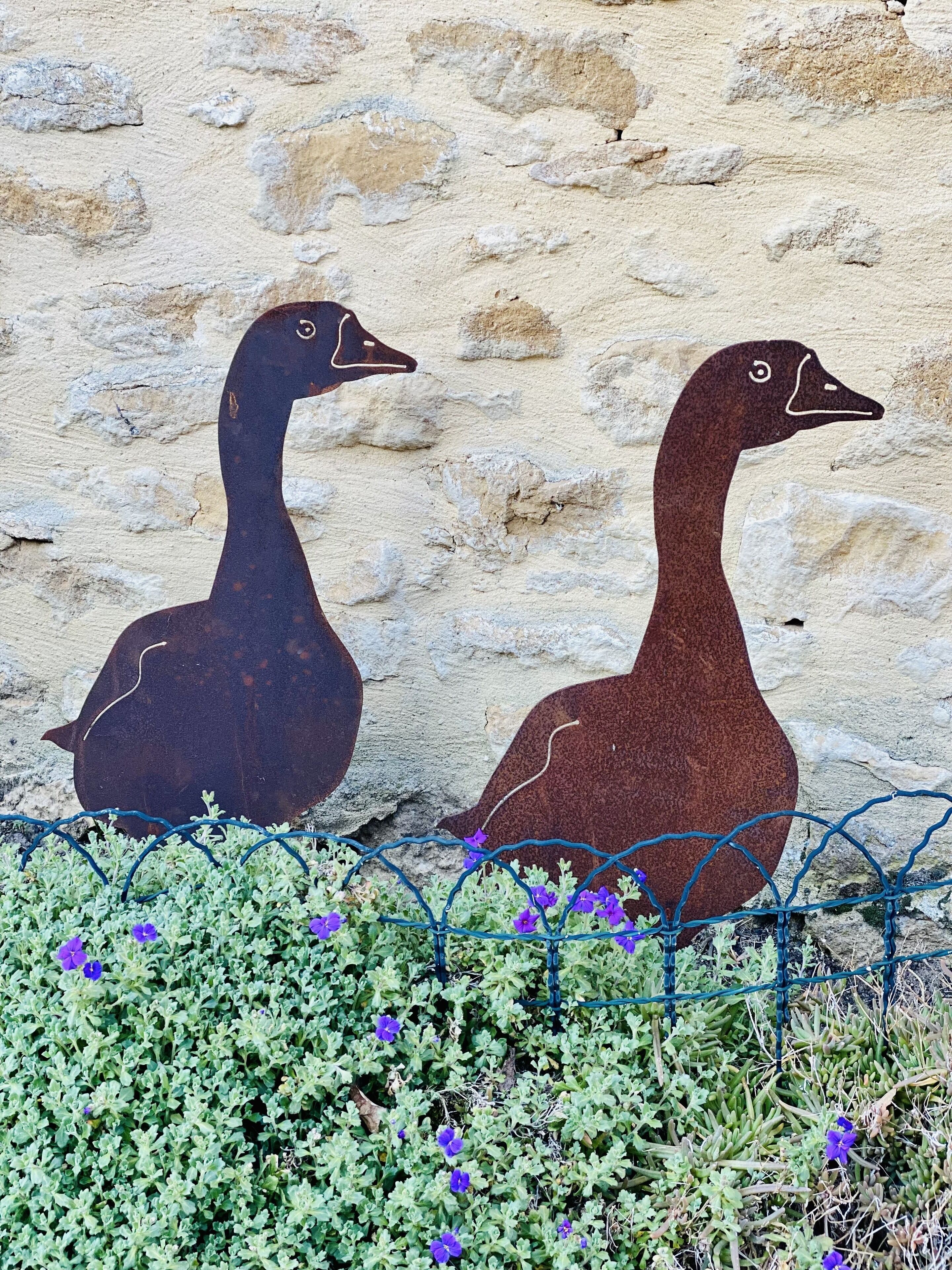 Two large, dark-colored sculptures of ducks against a textured stone wall.