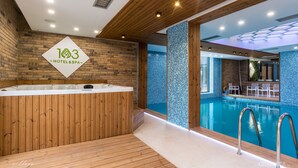 Een moderne hotelspa met een houten receptiebalie, een groot binnenzwembad en uitzicht op het zwembad.
