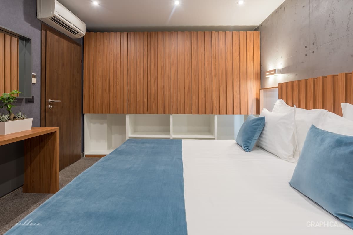 A modern bedroom with a wooden headboard, a large bed with blue and white bedding, and a small desk with a plant.