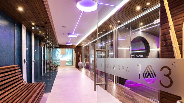 Een moderne hotellobby met een receptiebalie, houten banken en een bord met spa-informatie.