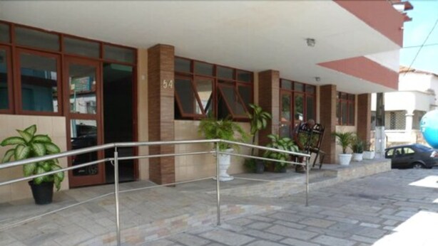 Entrada de hotel con un sendero adoquinado de piedra, baranda de metal y plantas en macetas.