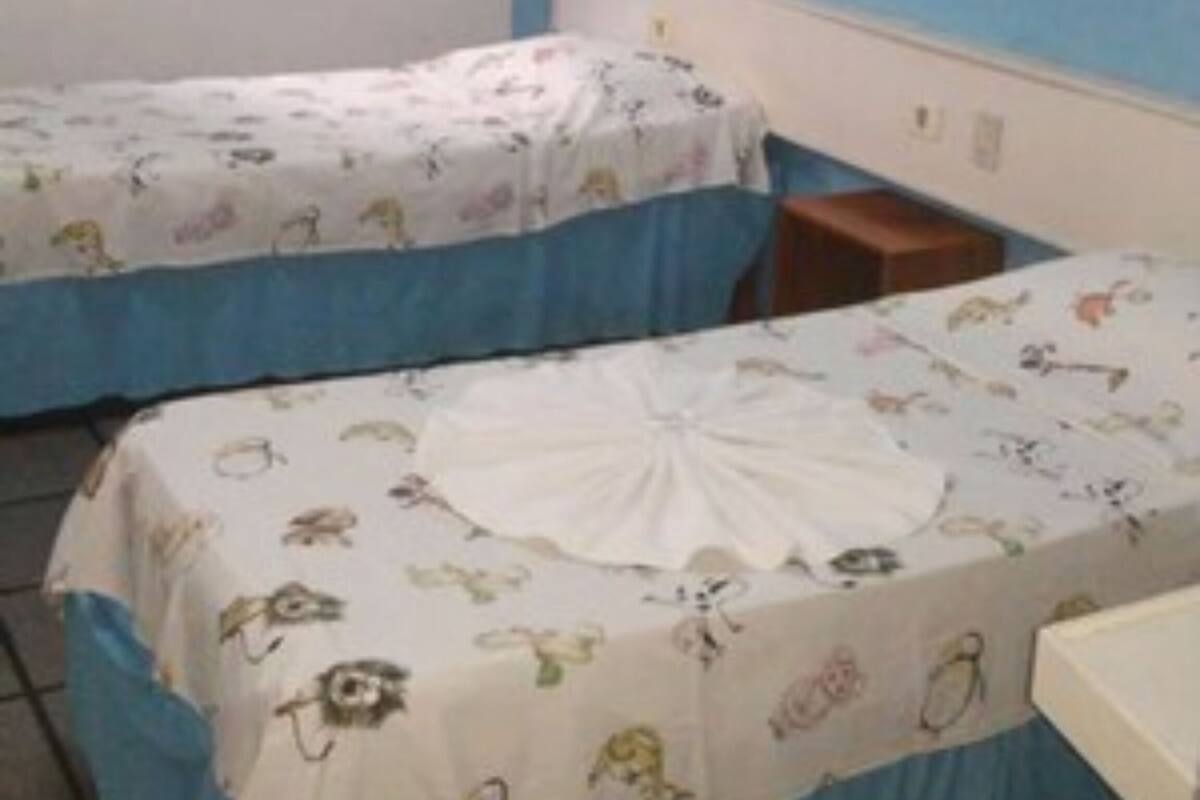 A room with two beds, a small table, a wall-mounted air conditioner, and a framed picture.