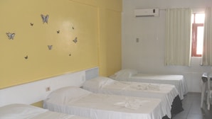 Habitación de hotel con tres camas individuales, una pared amarilla, adhesivos decorativos de mariposas, un equipo de aire acondicionado y una ventana con cortinas.
