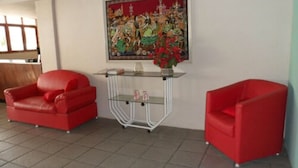 Una habitación con dos sillas rojas, una mesa de vidrio con un florero y un cuadro grande en la pared.