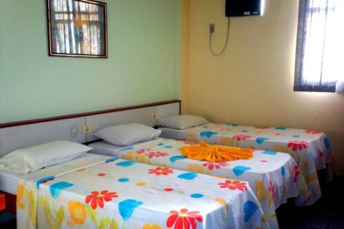 A hotel room with two beds, each with a floral bedspread and pillows. There is a television mounted on the wall and a window with curtains.