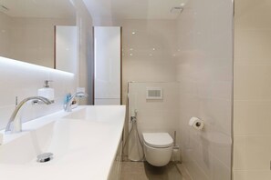 Et moderne badeværelse med en hvid vask, to haner, et toilet og et bruseområde.