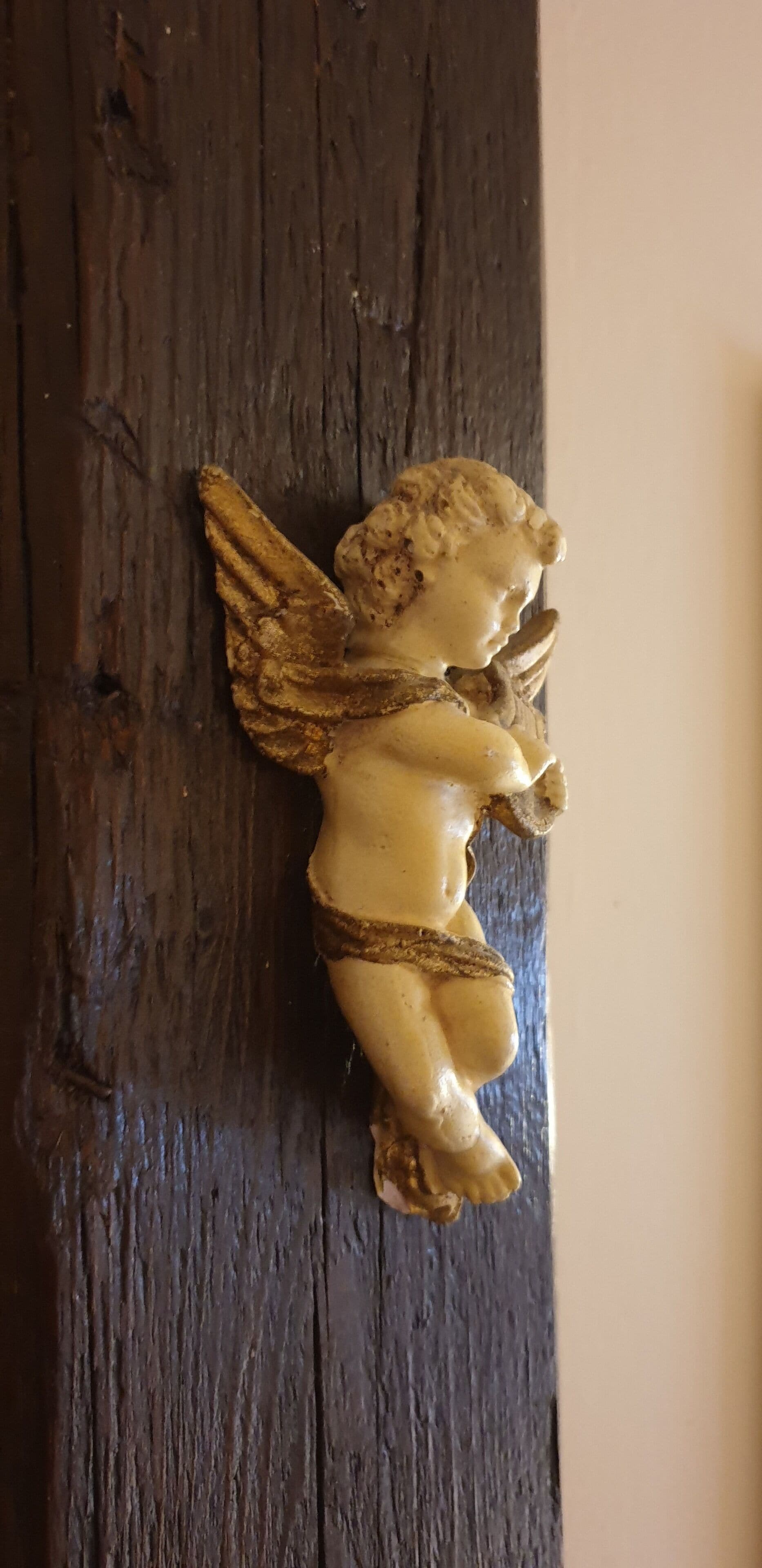 Eine kleine Engel-Figur an einer dunklen Holzfläche befestigt.