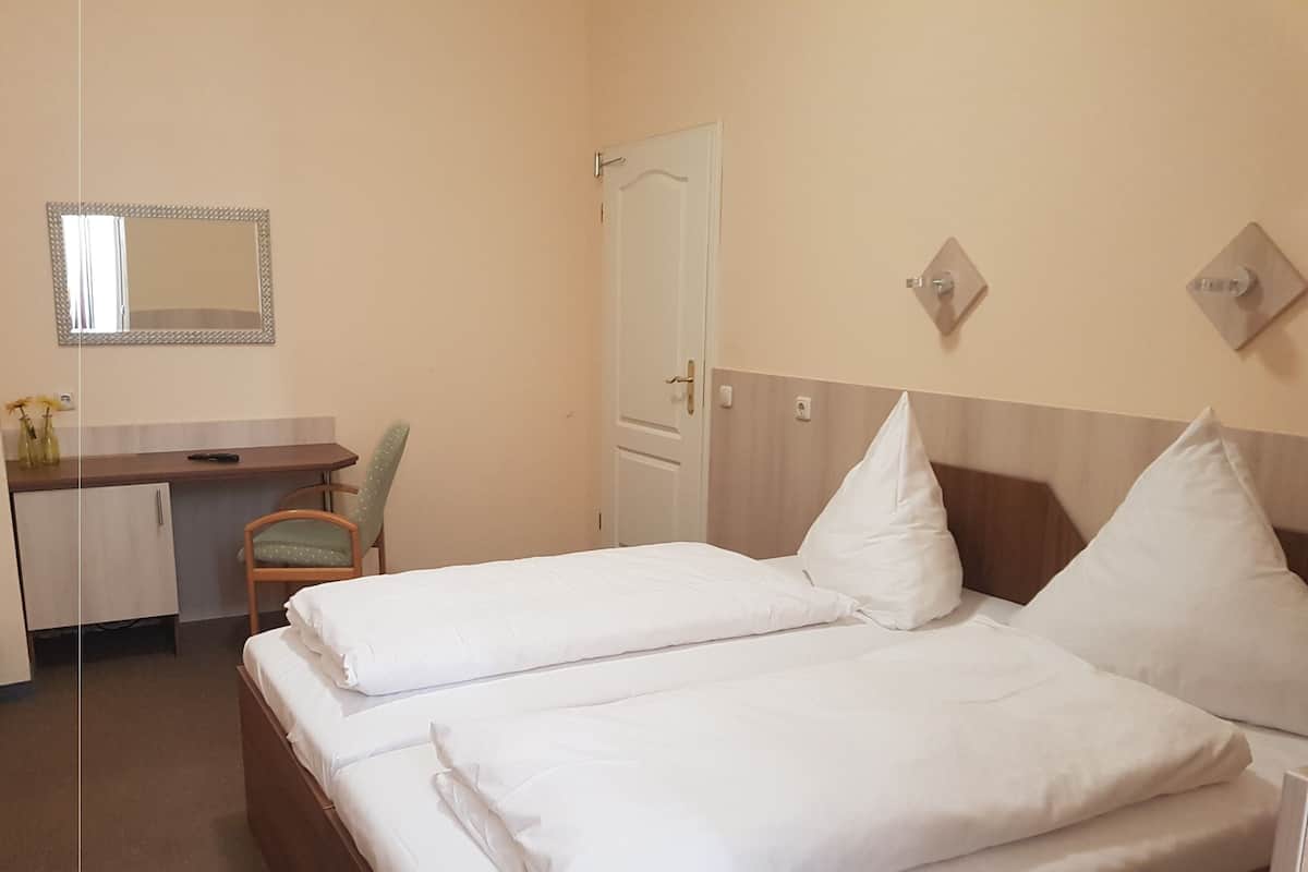 A hotel room with two beds, a desk, a chair, and a door.
