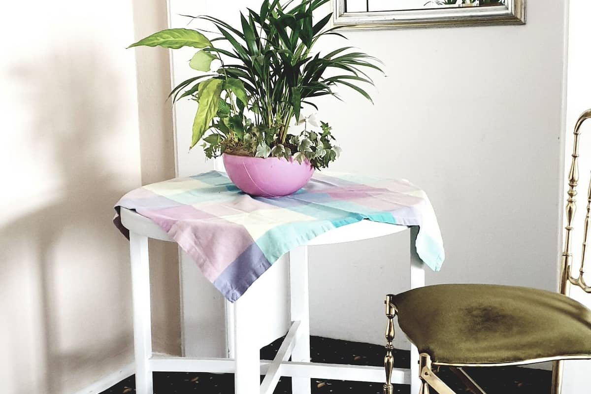 A corner with a white table, a green chair, a potted plant, and a mirror on the wall.