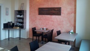 A dining area with a wooden table and chairs, a wall-mounted painting, and a shelf with glassware. - Pension Im Bett (Nuremberg)