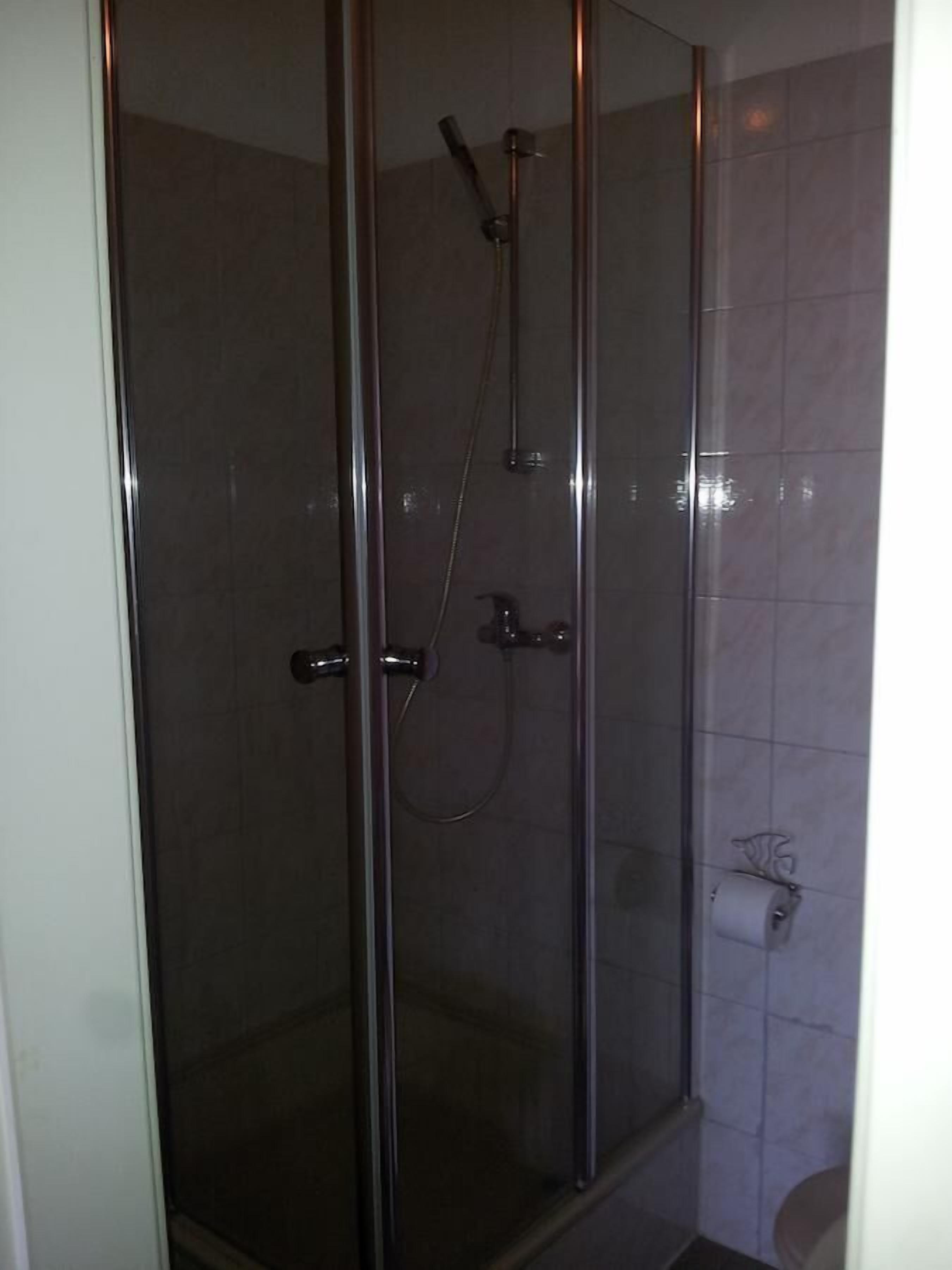 Cabina de ducha con paredes de vidrio, un cabezal de ducha manual y un grifo instalado en la pared.
