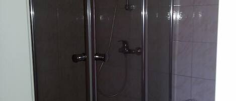 Cabina de ducha con paredes de vidrio, un cabezal de ducha manual y un grifo instalado en la pared.