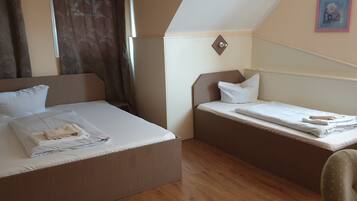 Ein Hotelzimmer mit zwei Betten, einem größeren und einem kleineren, beide mit weißer Bettwäsche. In der Ecke steht ein Sessel und ein kleiner Tisch.