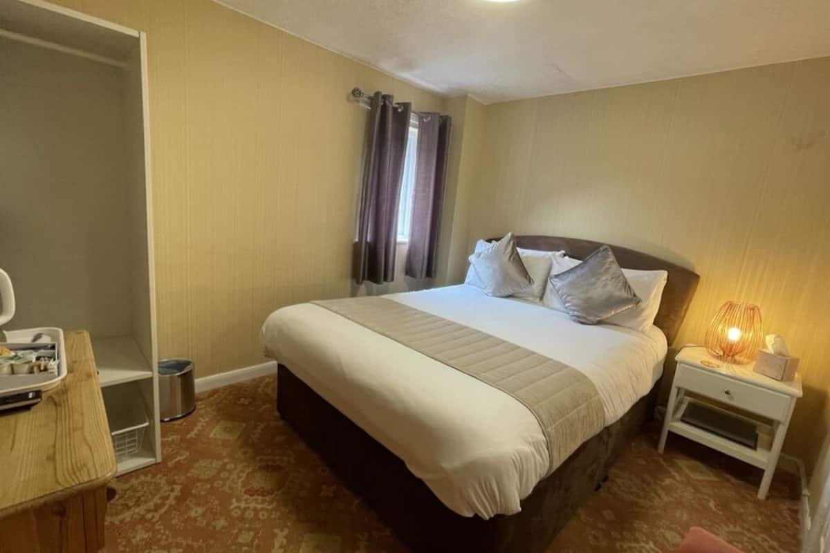 A hotel room with a bed, bedside table, lamp, and a wardrobe.