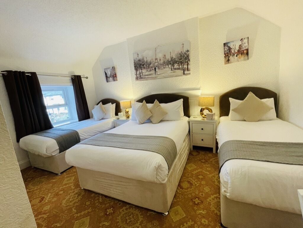 A hotel room with two beds, a small table, and a window with curtains.