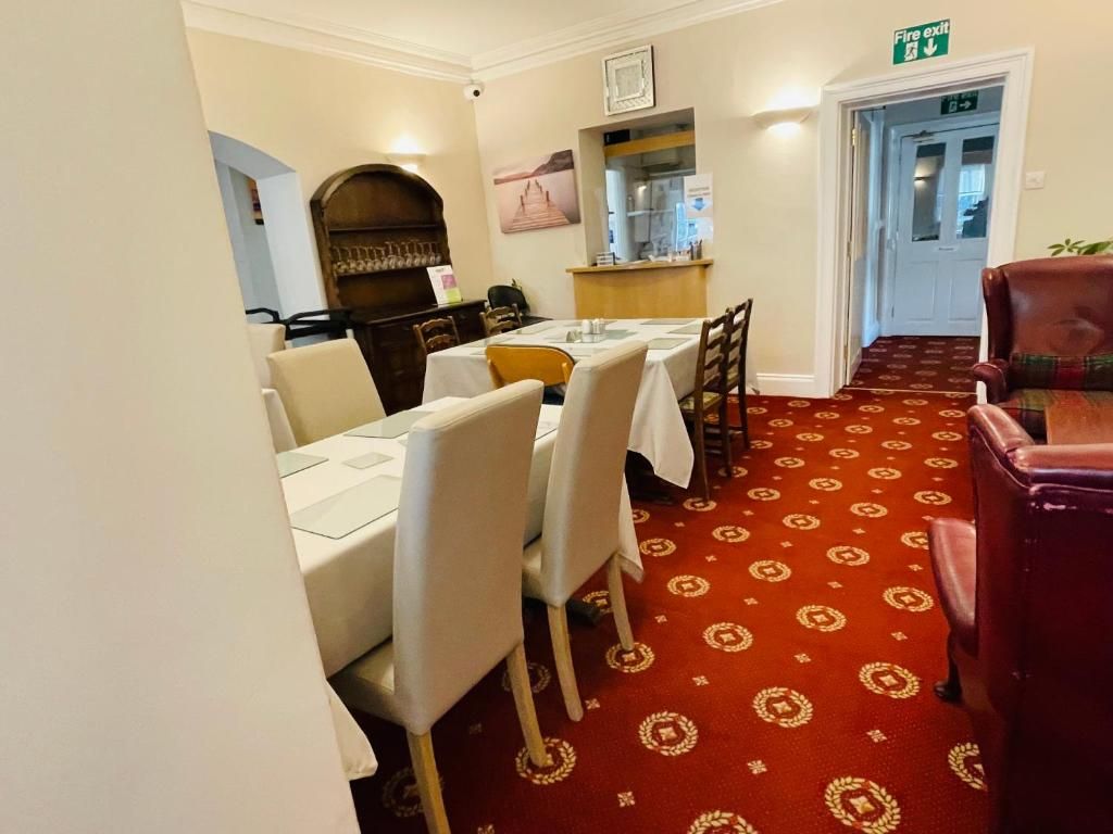 Un comedor de hotel con mesas dispuestas para los huéspedes, un letrero de salida de incendios y una alfombra estampada.