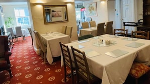 A dining area with tables set for service, a mirror on the wall, and a door leading to another room. - Fairlight Guesthouse (Penrith)