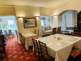Un comedor con mesas dispuestas para el servicio, un espejo en la pared y una puerta que da a otra habitación.