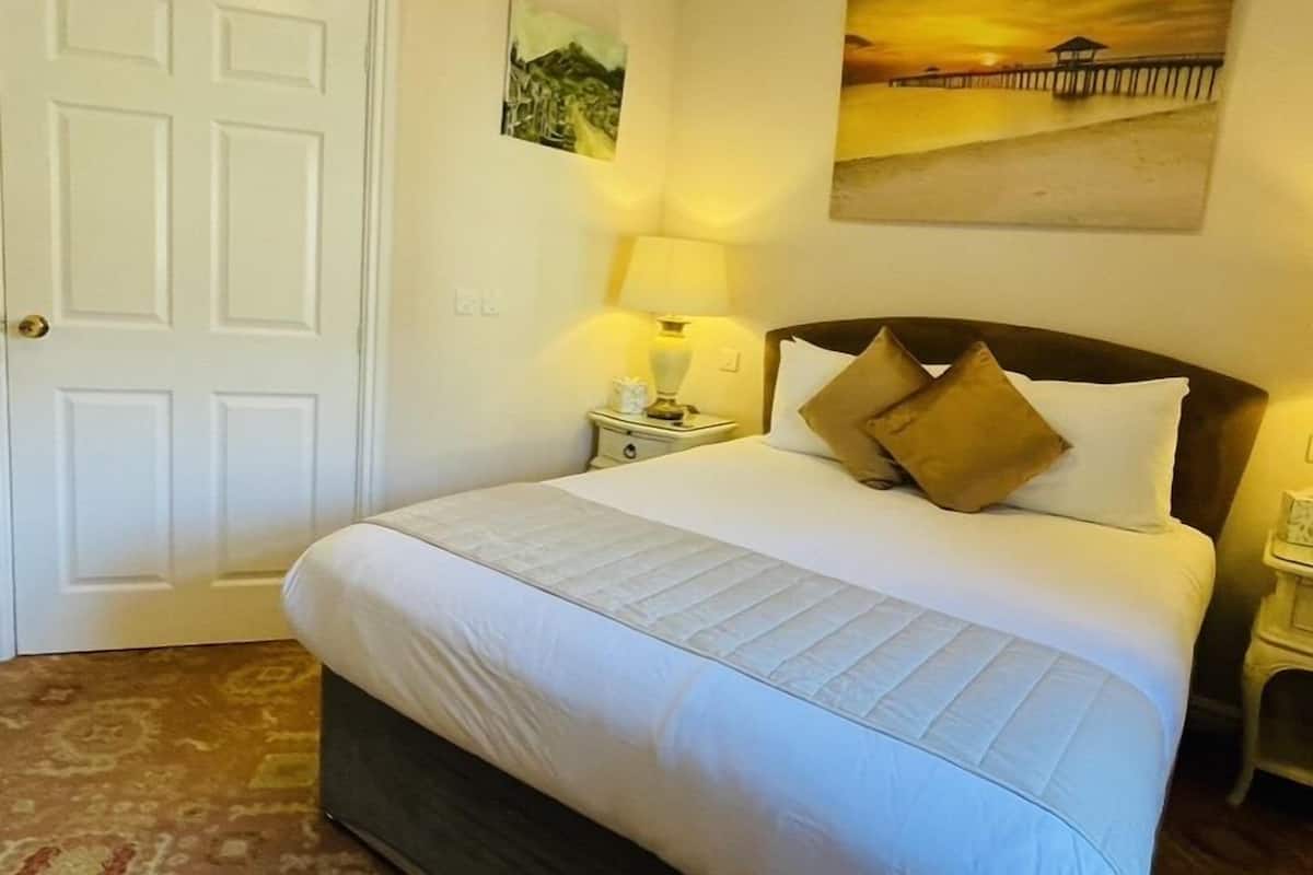 A neatly made bed with a headboard, a bedside lamp, and a painting on the wall.