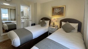 A hotel room with two beds, a bedside table with a lamp, a clock on the wall, and a framed picture. - Fairlight Guesthouse (Penrith)