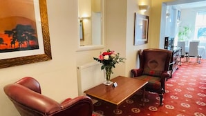 A hotel lobby with a red carpet, a wooden table with a vase of flowers, leather armchairs, and a framed painting on the wall. - Fairlight Guesthouse (Penrith)