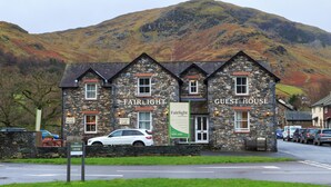 A stone building with 'Fairlight Cafe' and 'Guest House' signs, a parked white car, and a mountainous backdrop. - Fairlight Guesthouse (Penrith)