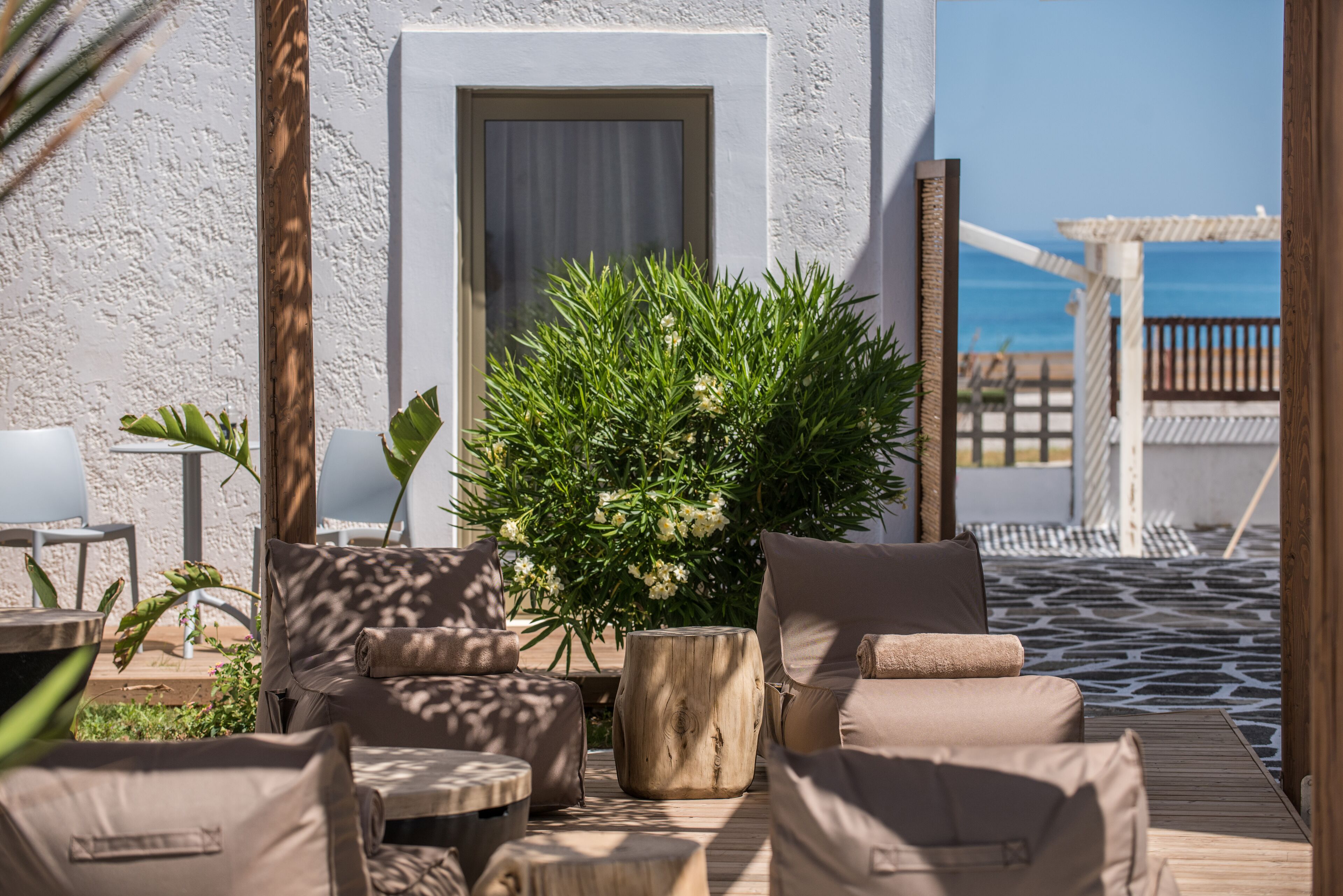 Ein sonnendurchfluteter Außenbereich mit Holzterrasse, einem Blumentopf und Blick aufs Meer.
