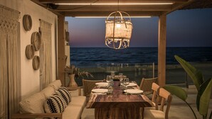 A dining area with a wooden table and chairs, a hanging light fixture, and a view of the ocean. - Enorme Maya Beach - Adults Only (Hersonissos)