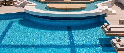 A pool area with a circular hot tub, lounge chairs, and a wooden deck.