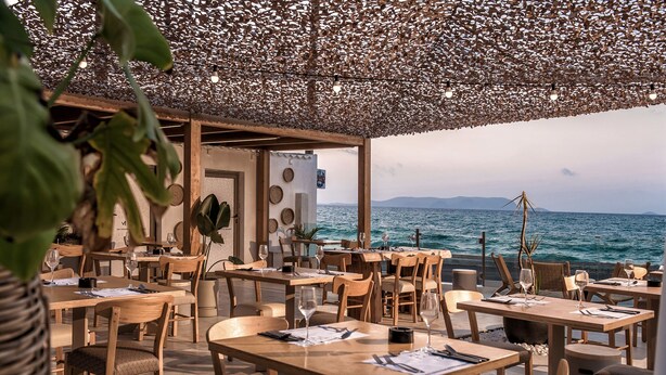 An outdoor dining area with wooden tables and chairs, a decorative ceiling, and a view of the sea. - Enorme Maya Beach - Adults Only (Hersonissos)
