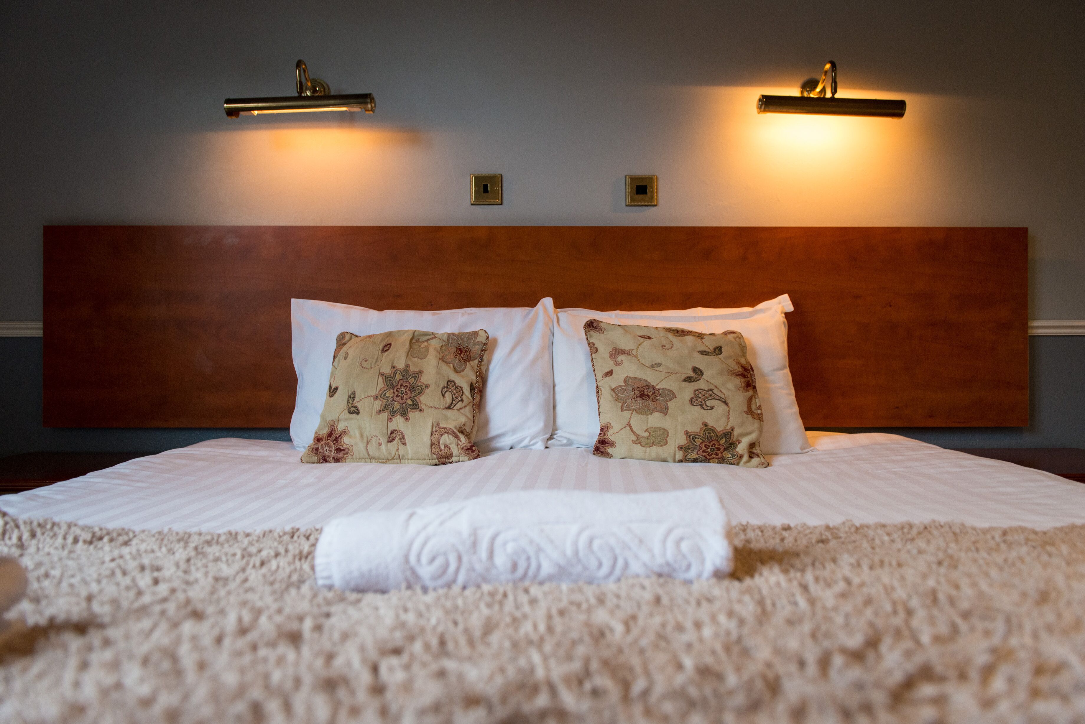 A neatly made bed with floral-patterned pillows, a matching throw, and a wooden headboard.